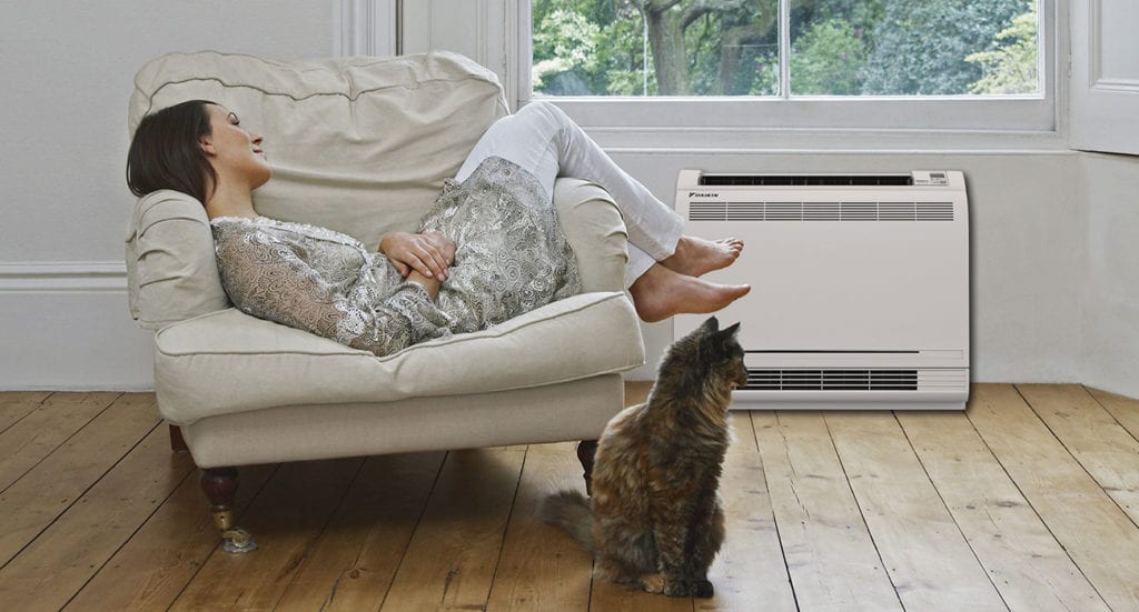 Woman sitting on chair next to cat and ductless mini split air conditioner.