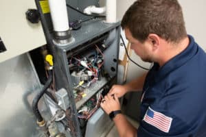 HVAC technician removing a panel from the front of a furnace in preparation for repair.