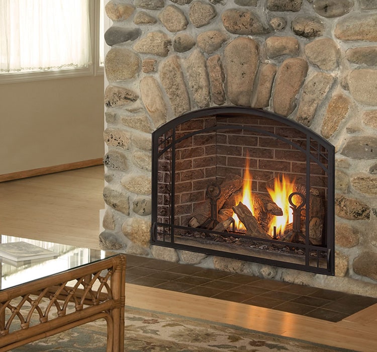 A fireplace roars inside a mantel with large stones. The living room is traditional with tan, beige and brown tones.