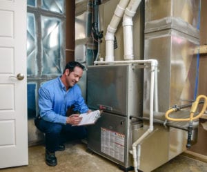 An HVAC technician smiles as he inspects a furnace in a home