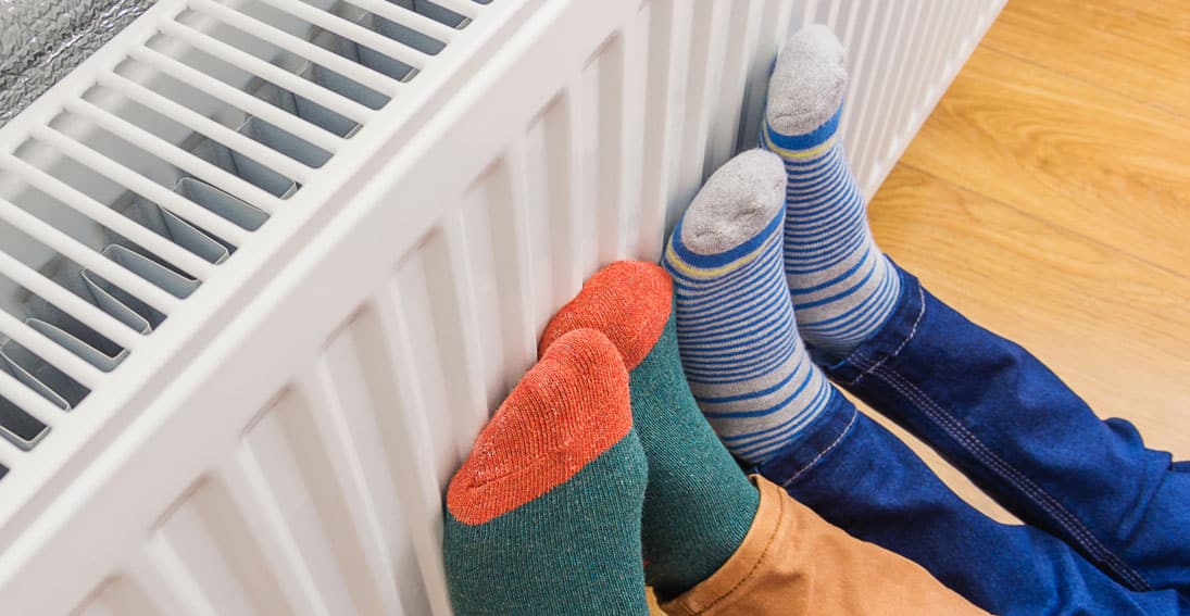 Two people wearing colorful socks warm their feet on a radiator