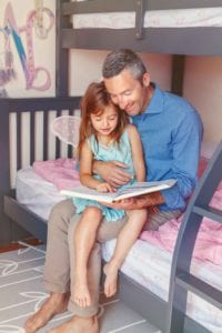 Father and daughter reading book together in child's bedroom.