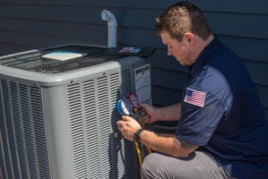 A male heating and cooling technician performs maintenance on a home air conditioner outdoors