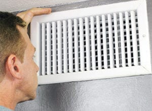 Man inspecting vent of home heating and cooling ductwork.