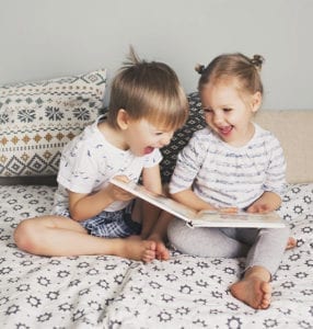 A young boy and girl laugh while they look at a picture book together