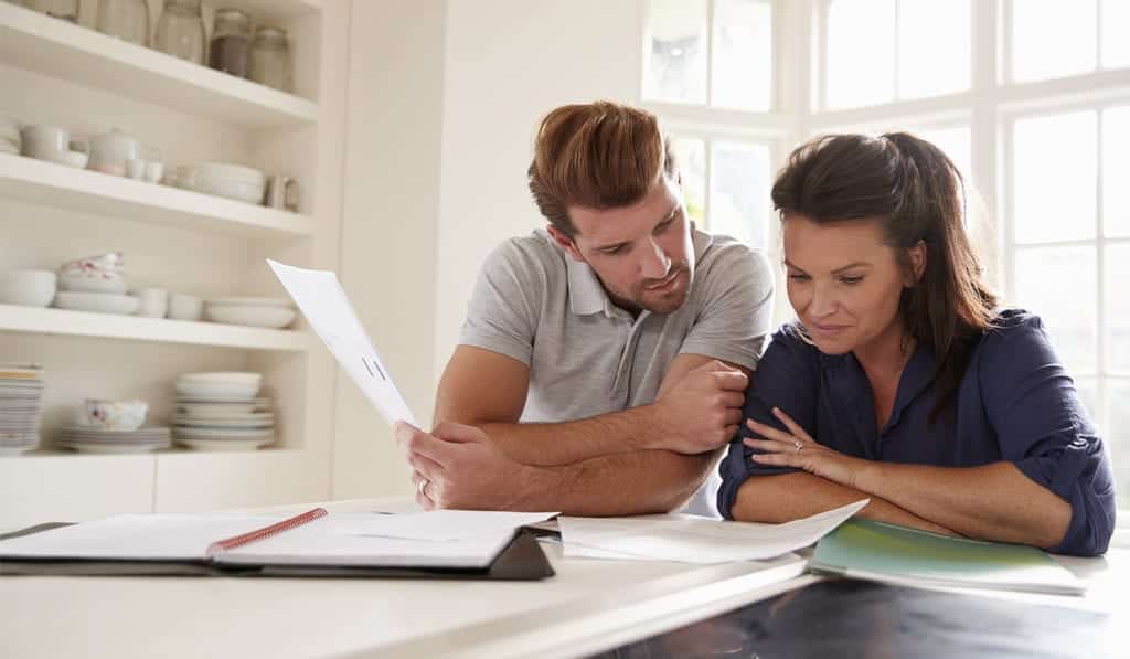 A husband and wife look over financial documents together in modern kitchen