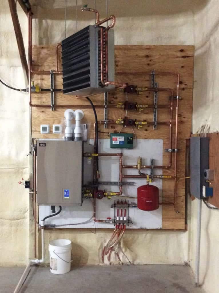 A modern home boiler hanging on a wooden wall surrounded by pipes