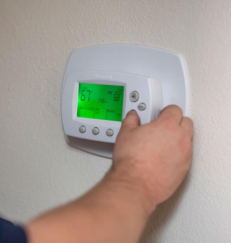 A closeup of a man’s hand adjusting a thermostat on a white wall in a home