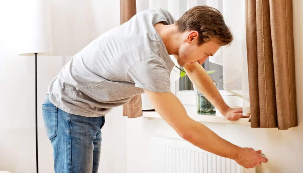 A young man adjusting the temperature on the radiator in his home
