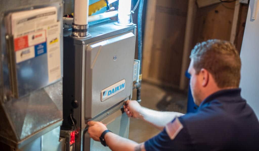 A male Bears Home Solutions heating and cooling technician removes the front panel of a Daikin furnace during an inspection