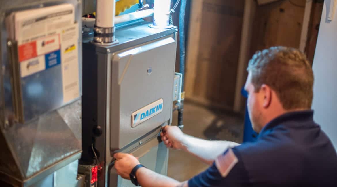 A male Bears Home Solutions heating and cooling technician removes the front panel of a Daikin furnace during an inspection