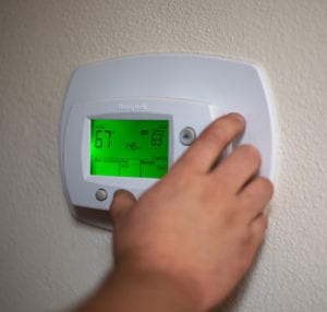 A closeup of a person’s hand adjusting a Honeywell thermostat on a white wall in a home