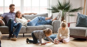 Parents relax on couch as they watch their kids play in their living room.