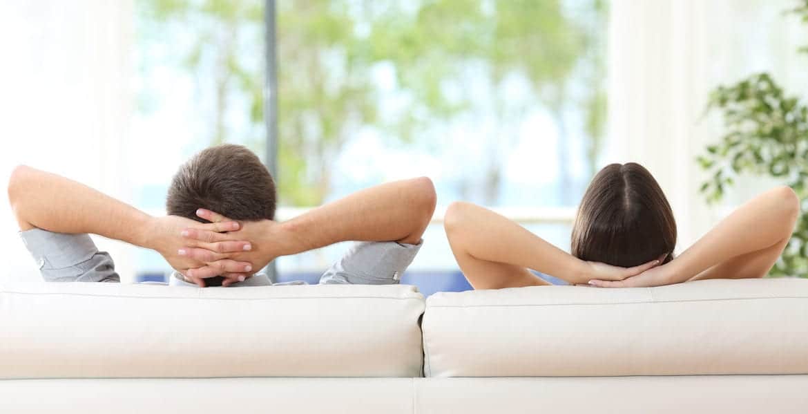 Two people resting on couch with hands behind their heads.