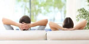 Two people resting on couch with hands behind their heads.