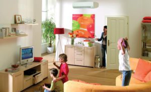 Three children playing in a modern living room while a mom adjusts the temperature on a ductless mini split air handler in the background