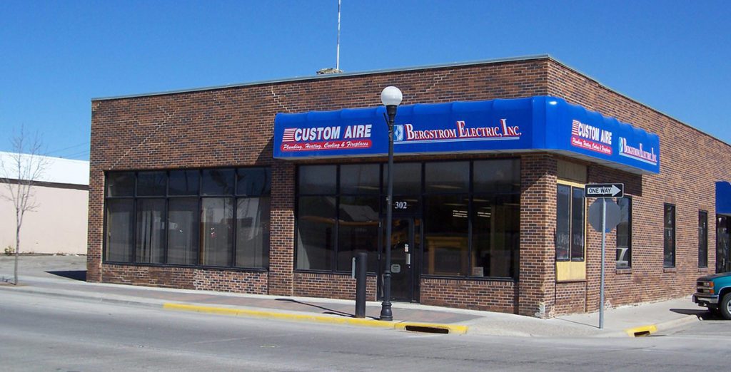 A brick building with a blue awning that has Custom Aire’s old red and white logo on it, as well as Bergstrom Electric, Inc.