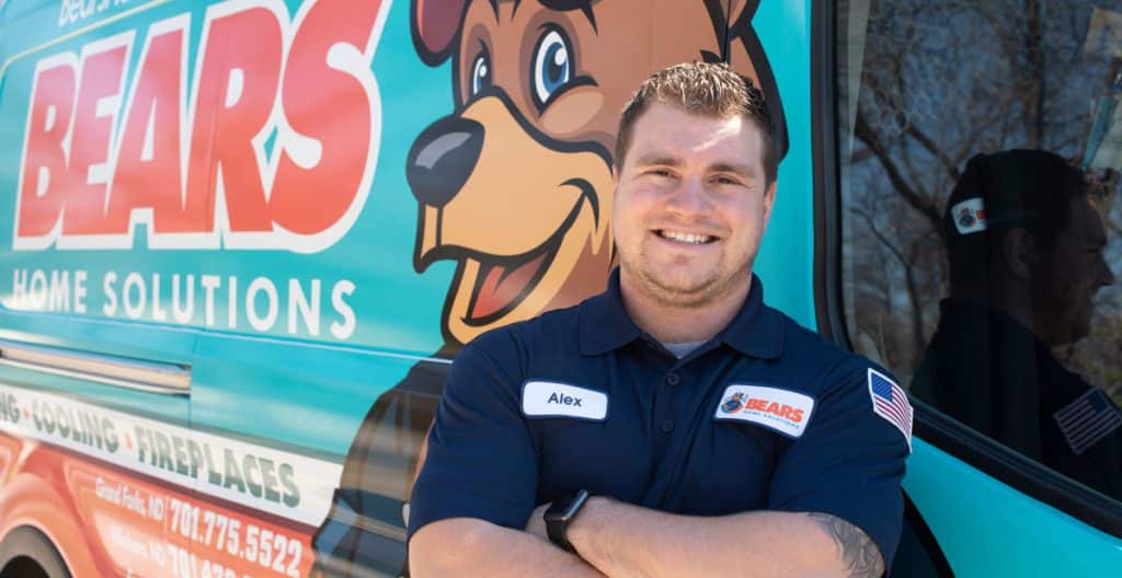 : A young male Bears Home Solutions HVAC service technician smiling for a photo in front of his service van.