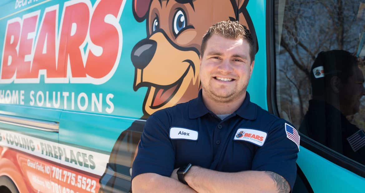 : A young male Bears Home Solutions HVAC service technician smiling for a photo in front of his service van.