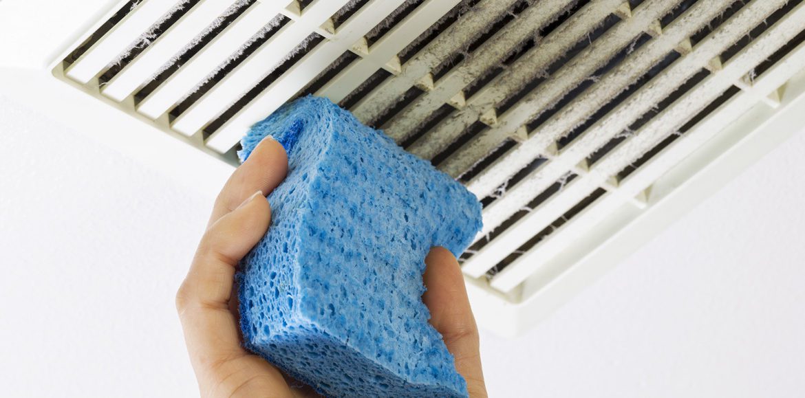 A closeup of a person cleaning a dirty return air vent with a sponge