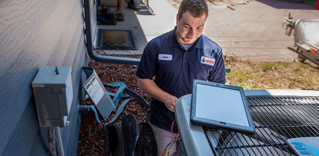 A young male HVAC installer for Bears Home Solutions works on a Daikin air conditioner in the backyard of a home