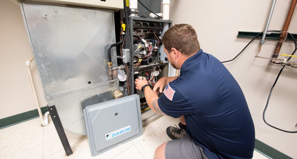 A male Bears Home Solutions HVAC service technician inspecting the inside of a Daikin home furnace