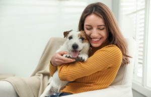 A young woman hugging her terrier puppy while sitting on a chair in her living room