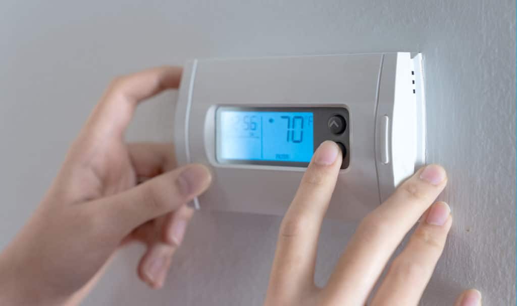 A closeup of a person's hands adjusting a digital thermostat in their home