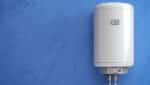 A modern tankless water heater hanging on a plain blue wall
