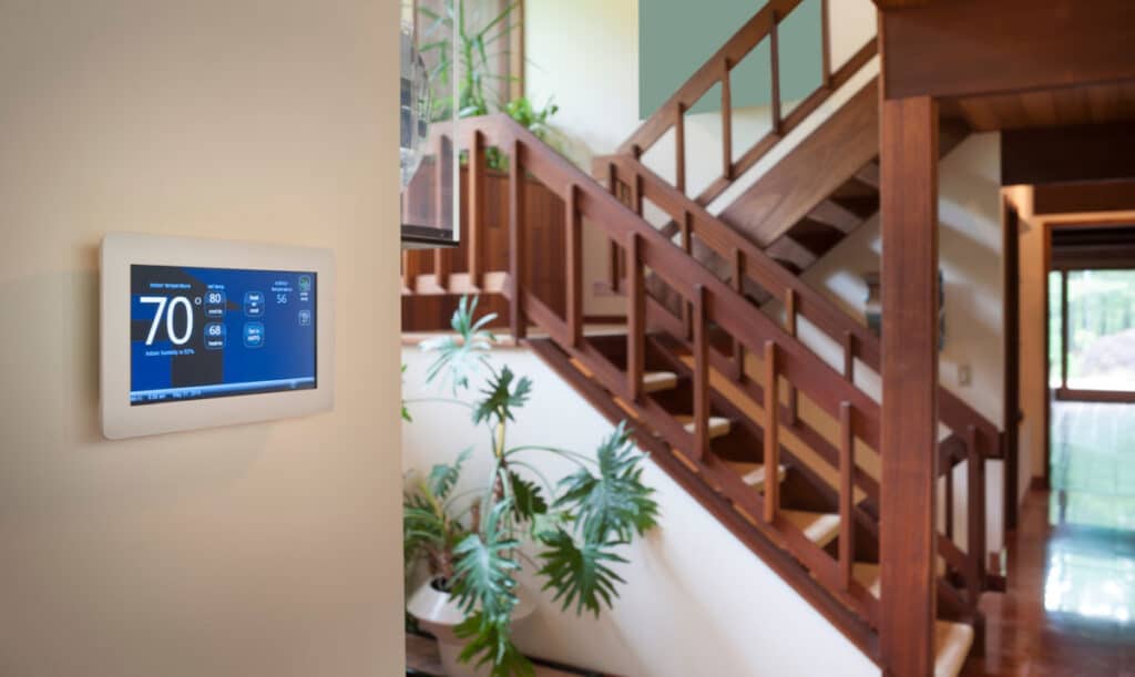 A smart thermostat with a wooden staircase in the background