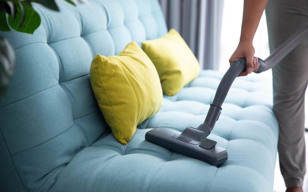 A person cleaning a couch with a handheld vacuum