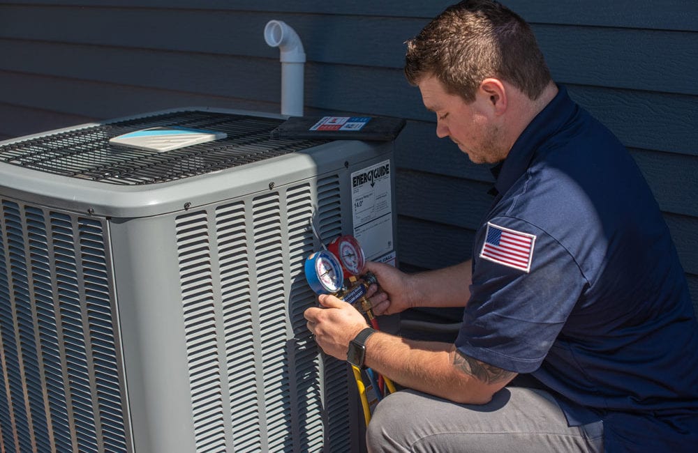A male heating and cooling technician performs maintenance on a home air conditioner outdoors