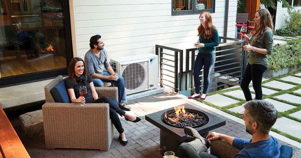 A group of friends socializing on a modern outdoor patio with a Daikin FIT unit in the background 