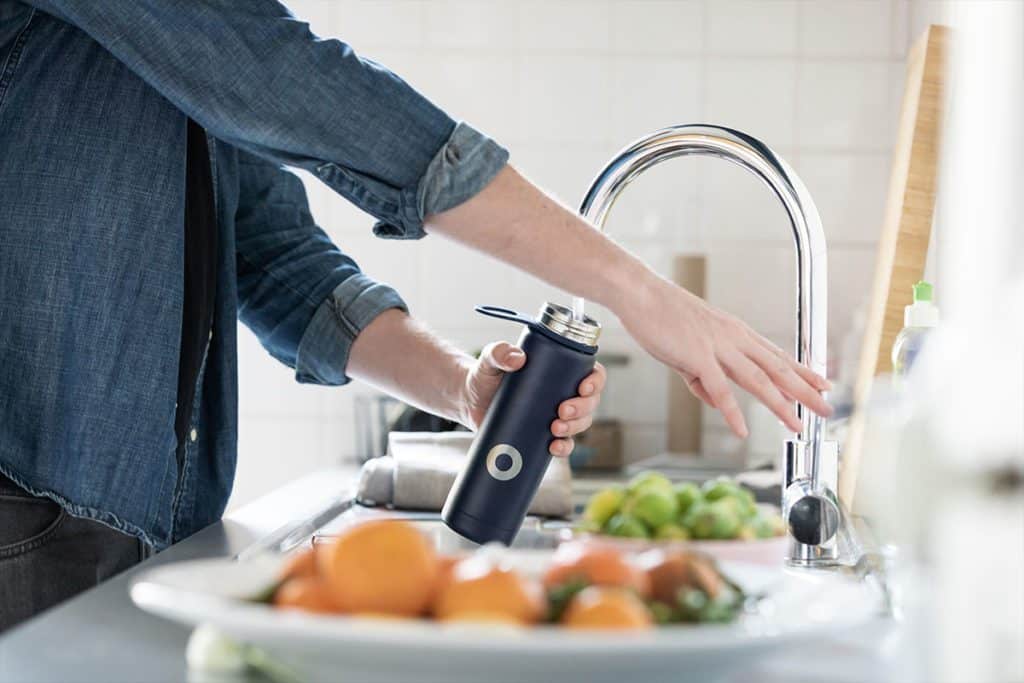 A close-up of a person filling up a reusable water bottle at a kitchen faucet 