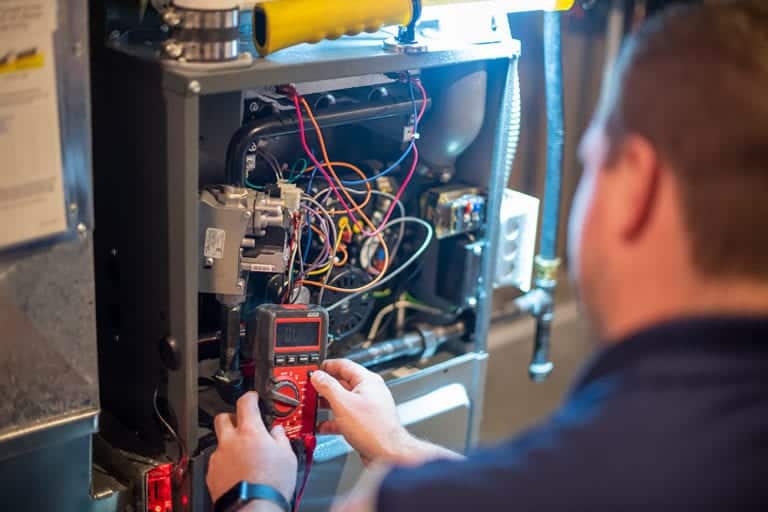 A male heating and cooling technician performs maintenance on a home air conditioner outdoors
