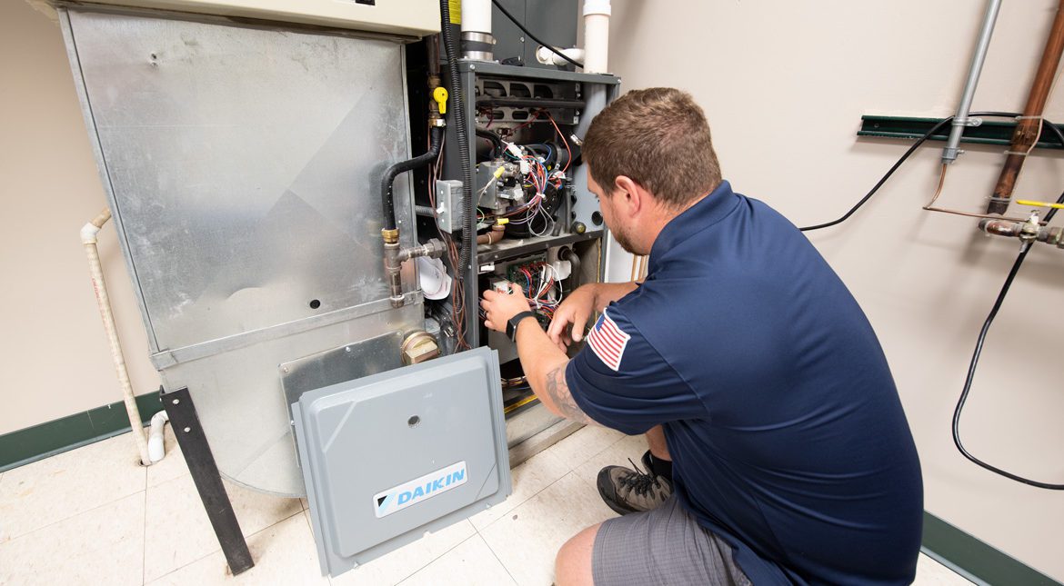 A male Bears Home Solutions HVAC service technician inspecting the inside of a Daikin home furnace